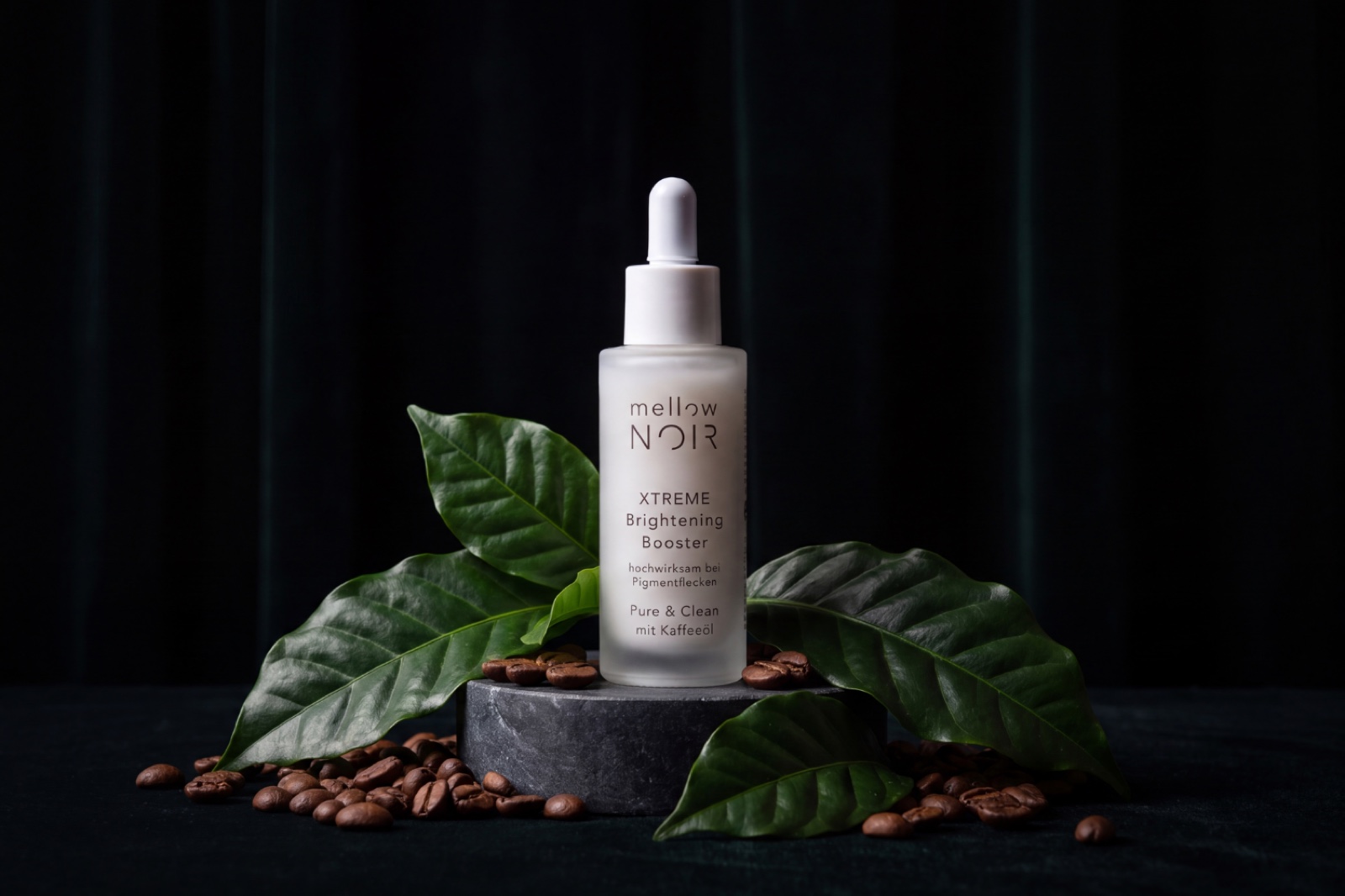 mellow NOIR XTREME Brightening Booster Flakon auf Schieferstein mit Kaffeepflanze und Kaffeebohnen